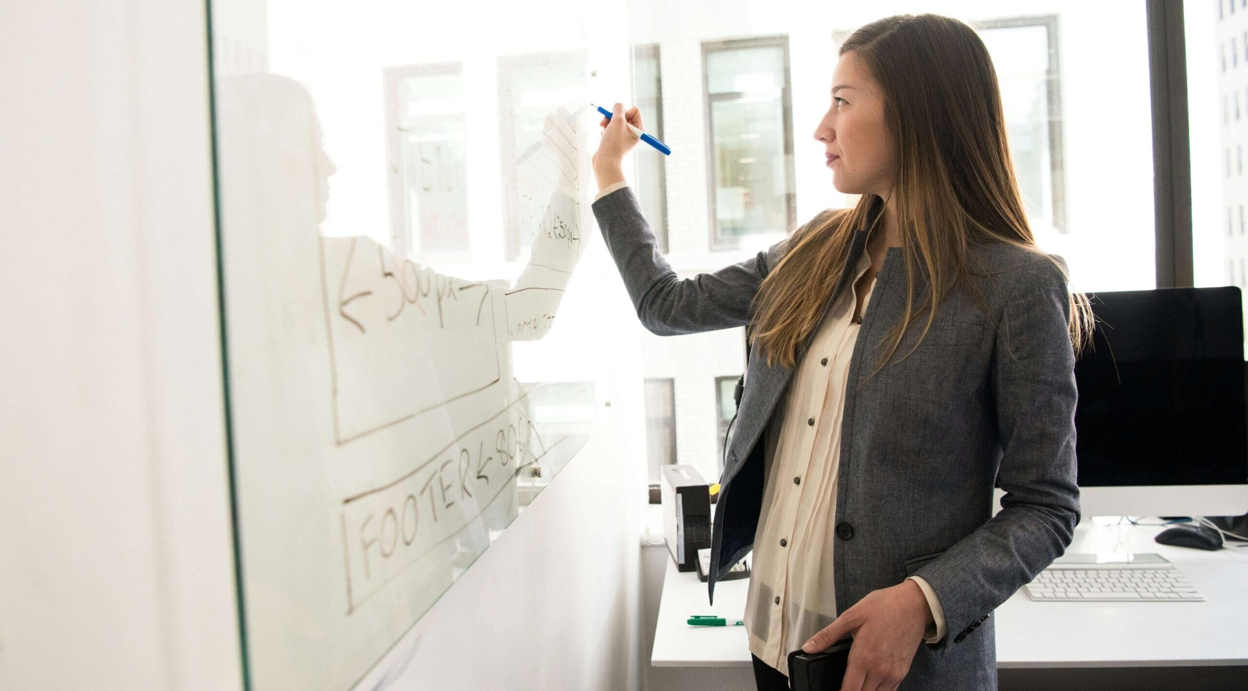 female designer standing in front of a white board sketching out development phases.