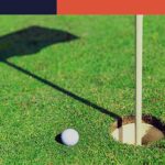 golf ball on the green next to hole with a shadow of the flag